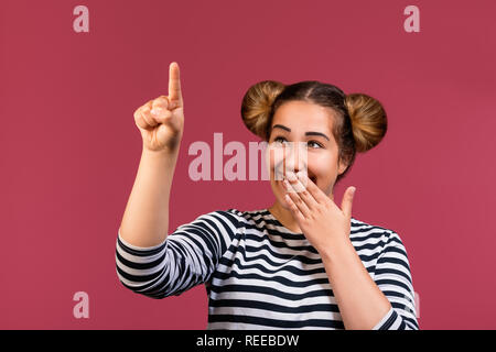 Giovani Funny Girl Teen coprire la bocca e puntare il dito pronto a scrivere, fare una presentazione o nuova idea, isolate su sfondo rosa Foto Stock