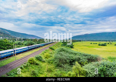 Vista spettacolare della ferrovia indiana che corre in pista va all'orizzonte in un paesaggio verde sotto il cielo blu con le nuvole. Foto Stock