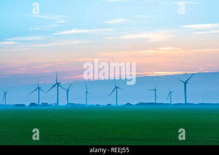 Il potere di vento UK, vista attraverso un Cambridgeshire fen verso una fila di turbine eoliche, Inghilterra, Regno Unito. Foto Stock