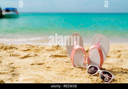 Rosa e Bianco sandali, occhiali da sole sulla spiaggia di sabbia in riva al mare a. Moda casual style flipflop e bicchieri al mare. La vacanza estiva sulla spiaggia tropicale. Foto Stock