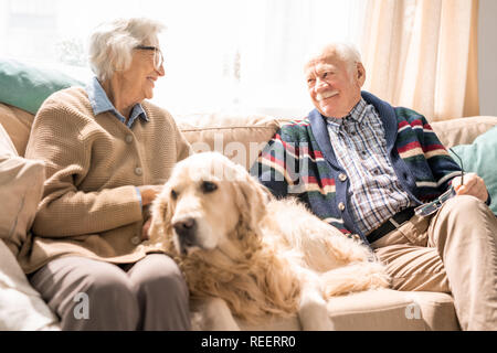 Ritratto di felice coppia senior con il cane seduto sul divano insieme e godendo il pensionamento Foto Stock