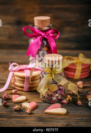 Amore con sfondo rosa rosa germogli per il tè in un barattolo di vetro a forma di cuore biscotti Foto Stock