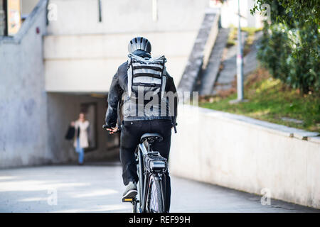 Una vista posteriore della bicicletta maschio corriere consegna di pacchi in città. Copia dello spazio. Foto Stock