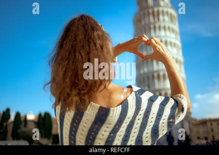 Visto da dietro il giovane donna in camicia a righe che mostra a forma di cuore le mani contro la torre pendente di Pisa, Italia. avente micro vacanze. non può evitare di cro Foto Stock