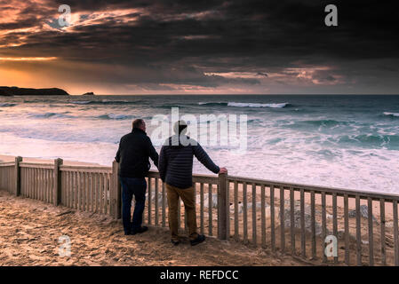 Due persone a guardare un tramonto spettacolare come nuvole temporalesche costruire su Fistral Beach in Newquay Cornwall. Foto Stock
