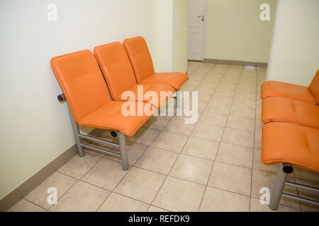 I posti vuoti in corrispondenza di un edificio aziendale contro un muro, impostazione interna.area di attesa con posti a sedere in una clinica.Empty orange sedie in sala d'attesa.Office Area entrata interni.hospital lobby con sedie per pazienti,visita medico. Foto Stock