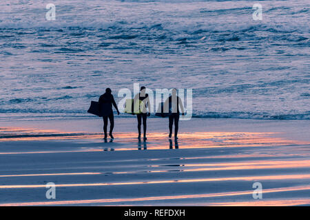 Tre surfisti corpo portante boogie boards visto in silhouette come il sole tramonta alle Fistral in Newquay Cornwall. Foto Stock