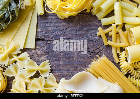 Telaio dalla varietà di tipi e forme di pasta italiana sul vecchio sfondo di legno dal di sopra. Cucina Italiana food concept e design del menu. Pasta secca b Foto Stock
