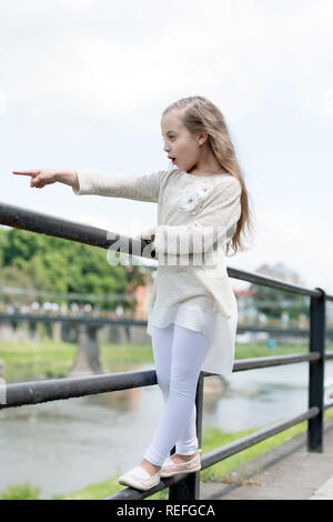 Kid ragazza con i capelli lunghi passeggiate nelle vicinanze Riverside, fiume sullo sfondo. Bambine Tourist Godetevi gite turistiche mentre passeggiate. Concetto di vacanza. Ragazza o schoolgirl in vacanza godere di viaggi ed escursioni. Foto Stock