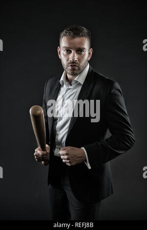 Imprenditore o un uomo in abito formale su sfondo scuro. Uomo sulla faccia di rigorosa in posa con la mazza di legno. Aggressivo il concetto di business. Uomo con setola guarda fiducioso e minaccioso. Foto Stock