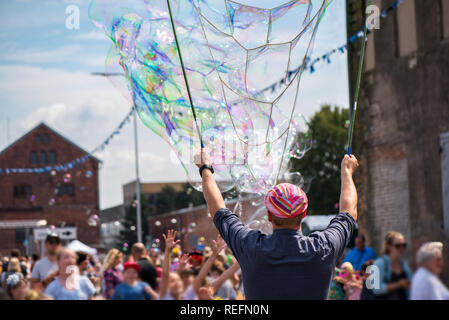 Un clown freelance soffiando centinaia di minuscoli, piccole e grandi bolle a festival all'aperto nel centro citta'. Concetto di intrattenimento, compleanni. I bambini aventi Foto Stock