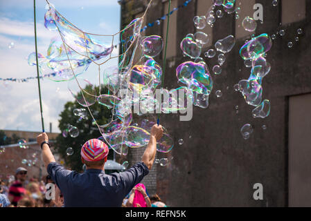 Un clown freelance soffiando centinaia di minuscoli, piccole e grandi bolle a festival all'aperto nel centro citta'. Concetto di intrattenimento, compleanni. I bambini aventi Foto Stock