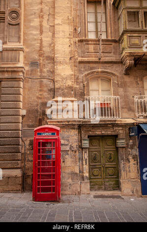 Inglese tradizionale telefono rosso casella al di fuori di un edificio barocco in Merchants Street a La Valletta, Malta. Foto Stock