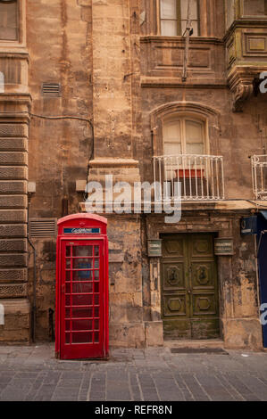 Inglese tradizionale telefono rosso casella al di fuori di un edificio barocco in Merchants Street a La Valletta, Malta. Foto Stock