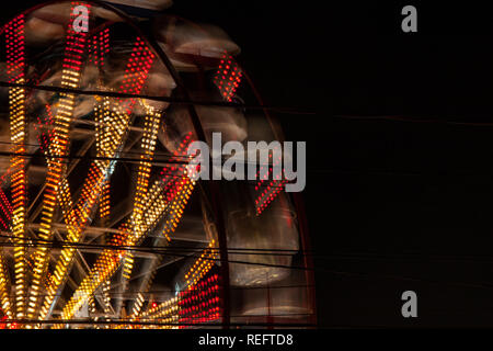 Sfondo di filatura ruota panoramica Ferris di colore giallo e con luci rosse in un parco di divertimenti di notte. N. persone. Foto Stock