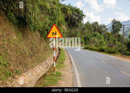 Segno tortuosa strada su una strada di montagna, avvertimento segno di traffico Vietnam Foto Stock
