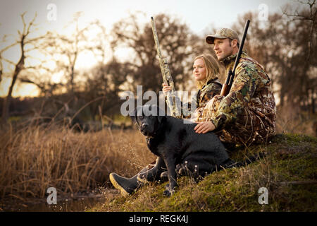 Giovane adulto giovane riprese di anatra con il loro cane da un lago al tramonto. Foto Stock