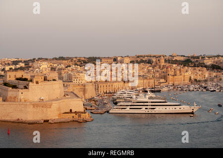 Vista da Upper Barrakka Gardens a La Valletta, Malta, oltre il Grand Harbour e il Forte Sant'Angelo con Vittoriosa Yacht Marina in serata calda luce del sole. Foto Stock