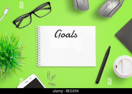 Gli obiettivi di scrittura sul blocco note il concetto di pagina. Green office desk con smart phone, bicchieri, cartella, caffè, impianto. Vista superiore della composizione. Foto Stock