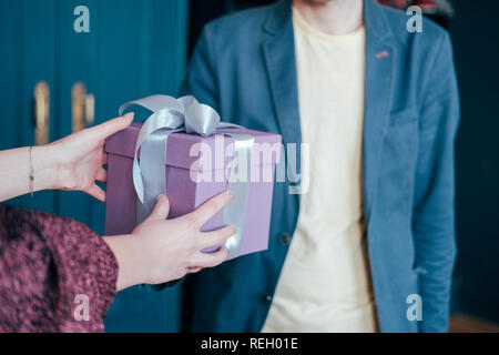 Donna a ottenere confezione regalo con il grigio argento nastro dal giovane uomo attracrive su sfondo blu Foto Stock