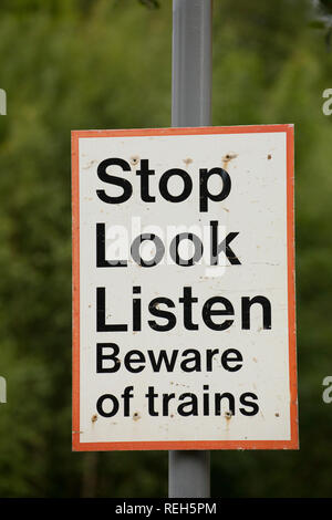 Un segno attenzione a guardare e ascoltare per treni accanto a un sentiero che attraversa una linea ferroviaria. Silverdale, Lancashire England Regno Unito GB Foto Stock