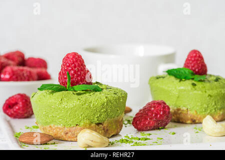 Verde matcha vegan torte raw con lamponi, menta, dadi e tazza di caffè per colazione. sano cibo delizioso. close up Foto Stock