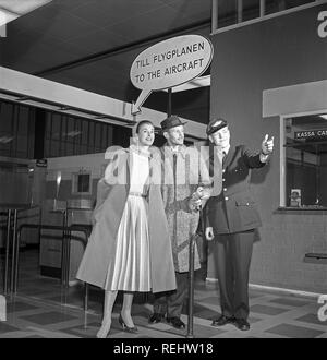 Matura negli anni cinquanta. Una giovane coppia in un aeroporto, pronti per la loro vacanza. Essi sono guidati al cancello di destra da un cordiale dipendente della compagnia aerea. Un segno sopra dice: Per l'aeromobile. La Svezia degli anni cinquanta. Foto Kristoffersson Ref CB15-8 Foto Stock