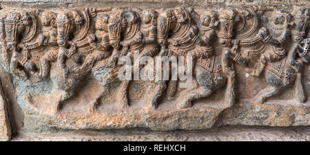 Belur, Karnataka, India - 2 Novembre 2013: Brown zoccolo in pietra scultura di fila di cavalli con i guerrieri li di equitazione al fondo del tempio di Chennakeshava Foto Stock