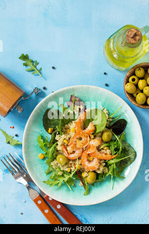 Menu dieta vegana, cibo. Una sana insalata con la quinoa, rucola, gamberi e olive su una pietra blu nella tabella. Vista superiore piatta sullo sfondo dei laici. Copia dello spazio. Foto Stock