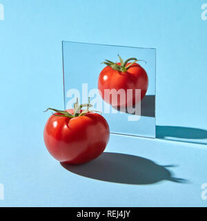 Pomodoro maturo con un gambo riflessa in uno specchio su sfondo blu con una copia dello spazio. Prodotto sano Foto Stock