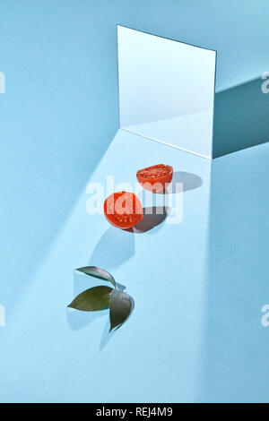 Metà di pomodori maturi, foglie verdi e un mirror su uno sfondo blu con copia spazio. Composizione alimentare Foto Stock