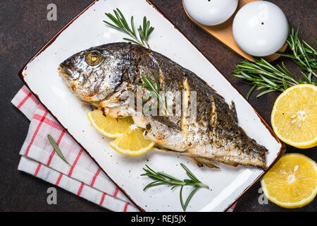 Dorado al forno pesce con limone e rosmarino su pietra scura tabella. Vista superiore, copia dello spazio. Foto Stock