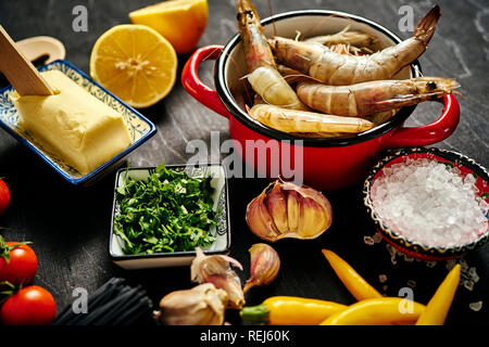 Fresche deliziose crude gamberoni in una pentola di rosso con prezzemolo, limone, burro, pomodori e peperoncino Foto Stock