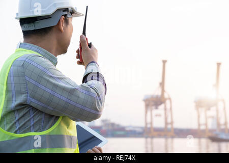 Uomo asiatico engineer radio e tablet e lavorando con contenitore merci nave in cantiere per la logistica Import Export sfondo, il controllo di sicurezza. E Foto Stock