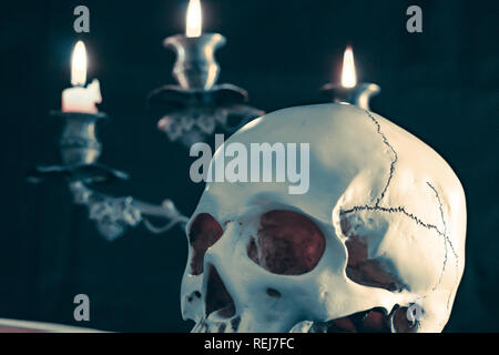 Illuminazione delle candele del cranio con candela e libri sulla scrivania in legno decorare per tema Halloween con copia spazio. Still Life immagini e messa a fuoco selettiva Foto Stock