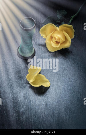 Rosa gialla accanto al piccolo vaso blu sul tavolo in legno con effetto di irraggiamento solare Foto Stock