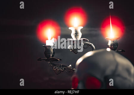 Illuminazione delle candele del cranio con candela e libri sulla scrivania in legno decorare per tema Halloween con copia spazio. Still Life immagini e messa a fuoco selettiva Foto Stock