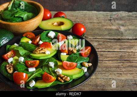 Insalata fresca con avocado, spinaci, pomodori ciliegia, il formaggio feta e noci in una piastra su tavola in legno rustico. cibo sano. close up Foto Stock