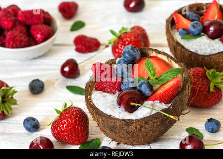 Budino di chia con frutti di bosco freschi, dadi, avena e menta in ciotole di cocco. Colazione sana. close up Foto Stock