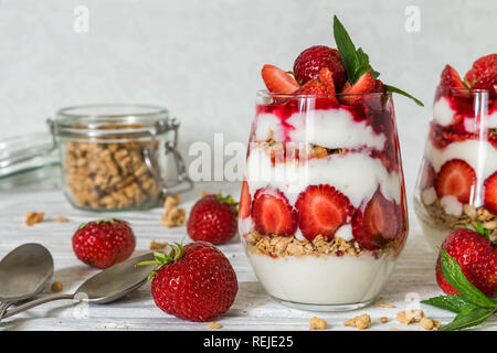 La frutta sana parfait di yogurt con muesli, menta e lamponi freschi in bicchieri bianco su un tavolo di legno. una sana prima colazione Foto Stock