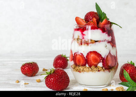 Yogurt fatto in casa parfait con granola e fragola in un vetro bianco su un tavolo di legno. una sana prima colazione Foto Stock