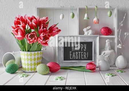 Primavera sfondo con decorazioni di Pasqua e una scheda di gesso. Espositore con diversi oggetti e tulipani rosa. Testo 'Felice Pasqua' a bordo. Foto Stock