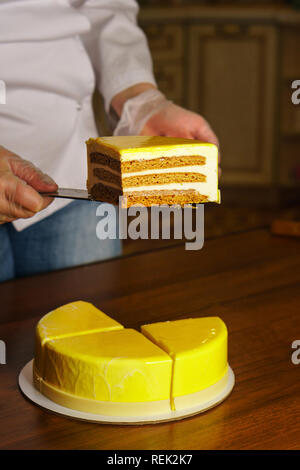 Tagli di pasticceria torta di miele in smalto con mirroring. Cucina casalinga. La donna trattiene il coltello pezzo di torta. Foto Stock
