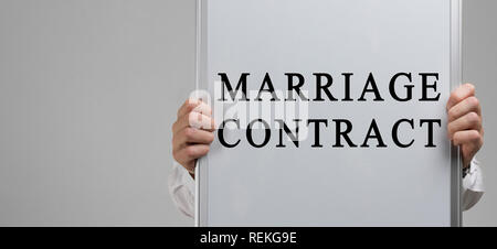 Gli uomini con le mani in mano tenendo un poster con la scritta contratto di matrimonio isolato su sfondo chiaro Foto Stock