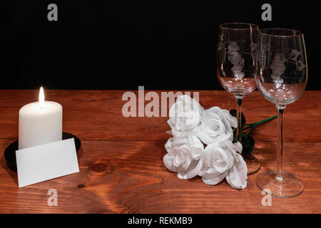 Bella inciso bicchieri di vino con rose bianche e bianco candela ed etichetta con il nome sul tavolo di legno e uno sfondo scuro. Valentines, Festa della Mamma, Pasqua, Chr Foto Stock