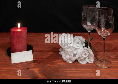 Bella inciso bicchieri di vino con awhite rose e candela rossa e il nome tag su un tavolo di legno e uno sfondo scuro. Valentines, Festa della Mamma, Pasqua, Chri Foto Stock