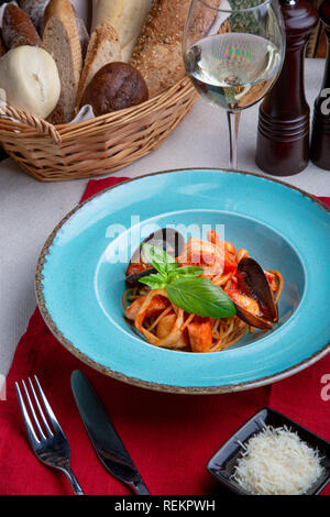 Cucina Italiana. Pasta con pesce e frutti di mare, i pomodori e il formaggio in un blu, una forchetta e un coltello su uno sfondo luminoso. Foto Stock