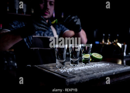 Aperitivo con gli amici nel bar, tre bicchieri di alcool con calce e sale per la decorazione. Scatti di tequila, il fuoco selettivo Foto Stock