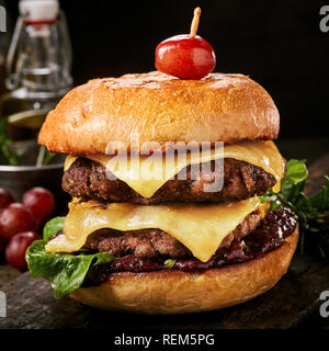 Close-up di un gustoso doppio hamburger con formaggio e fritti la carne di suolo su un tavolo di legno su sfondo nero con spazio di copia Foto Stock