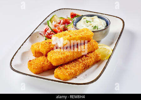 Studio shot close-up di gustose le dita di Pesce fritte servite con verdure e salsa tartare su un vassoio metallico su sfondo bianco per lo spazio di copia Foto Stock